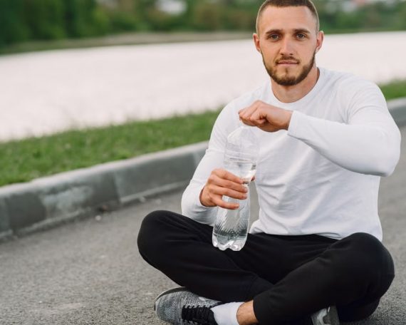 Man sitting on a road side, taking a break with a water bottle during an outdoor workout.