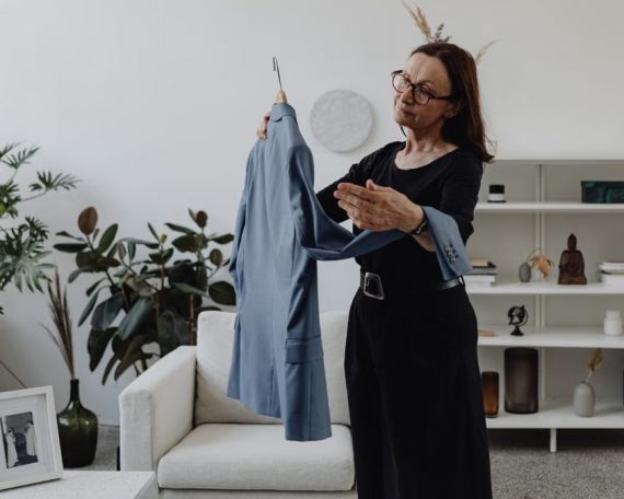 A woman in a modern living room holding a blue suit jacket pensively.